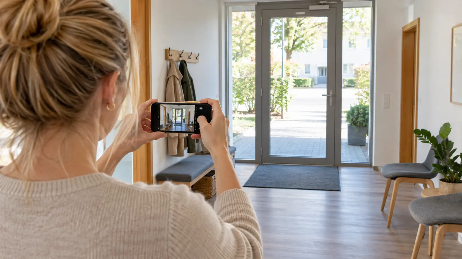 Eine Mitarbeiterin fotografiert mit dem Smartphone den leeren Eingang einer Therapiepraxis.