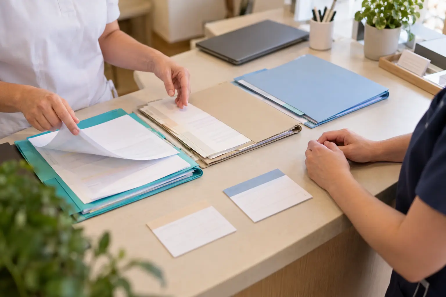 Am Empfangstisch besprechen zwei Mitarbeitende drei getrennte Dokumentenmappen und zwei Kalenderkarten beim Dienstwechsel.