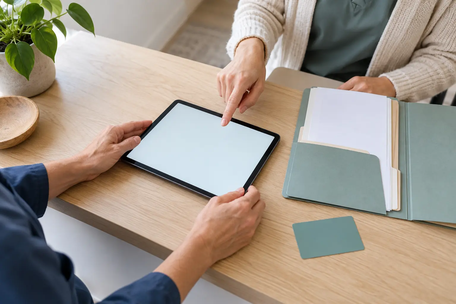 Hände zweier Personen am Tablet neben einer offenen Organisationsmappe.